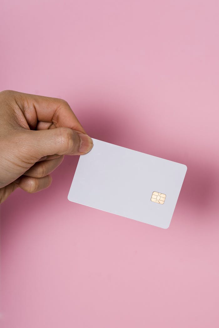 A hand holding a blank white SIM card on a vibrant pink background, showcasing technology.